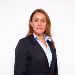 GERENTE REGIONAL CALDAS DPS GERENTE REGIONAL CALDAS: Retrato de estudio a medio cuerpo de una mujer con cabello castaño claro y liso, peinado hacia atrás. Viste un traje de chaqueta azul marino sobre una blusa azul claro con cuello. La mujer mira directamente a la cámara con una expresión neutra. El fondo es de color blanco sólido.